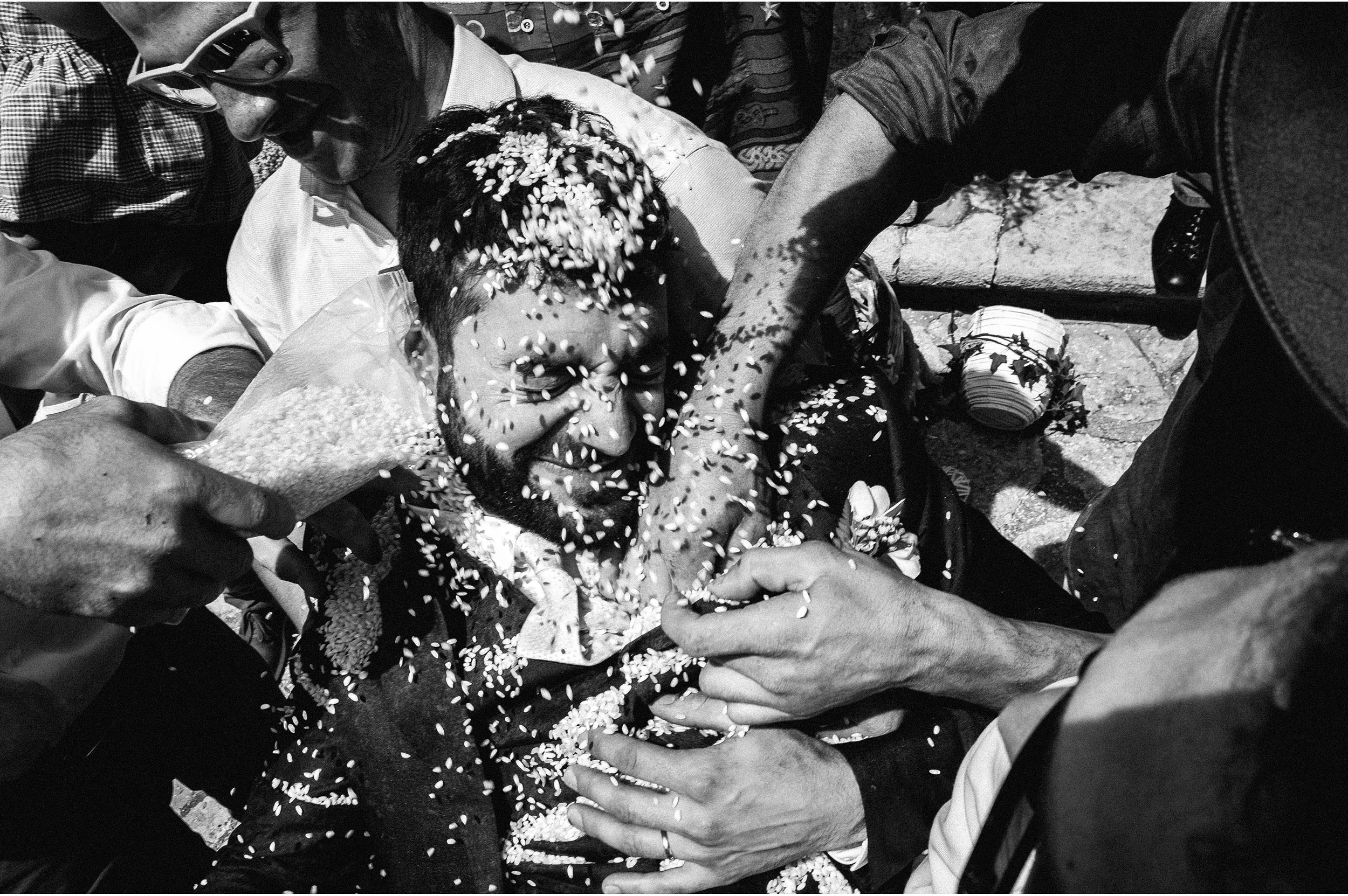 grooms friends stuff him up with rice outside the church black and white wedding photography
