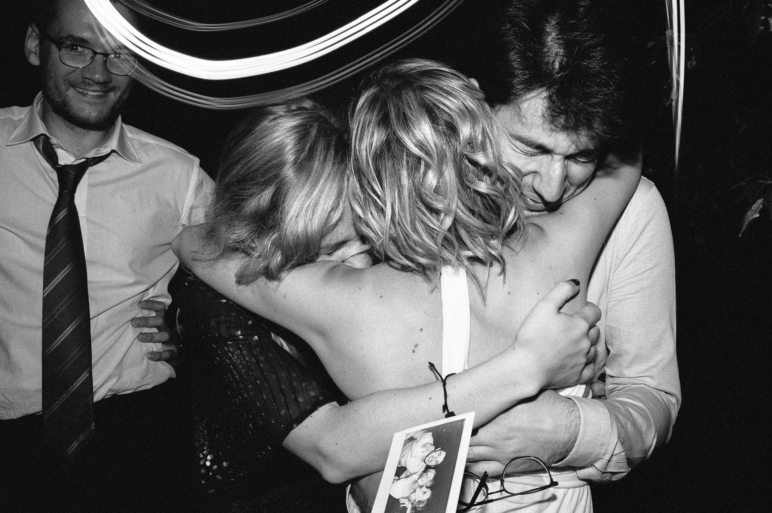 friends hug the bride after showing her their polaroid together black and white wedding photography