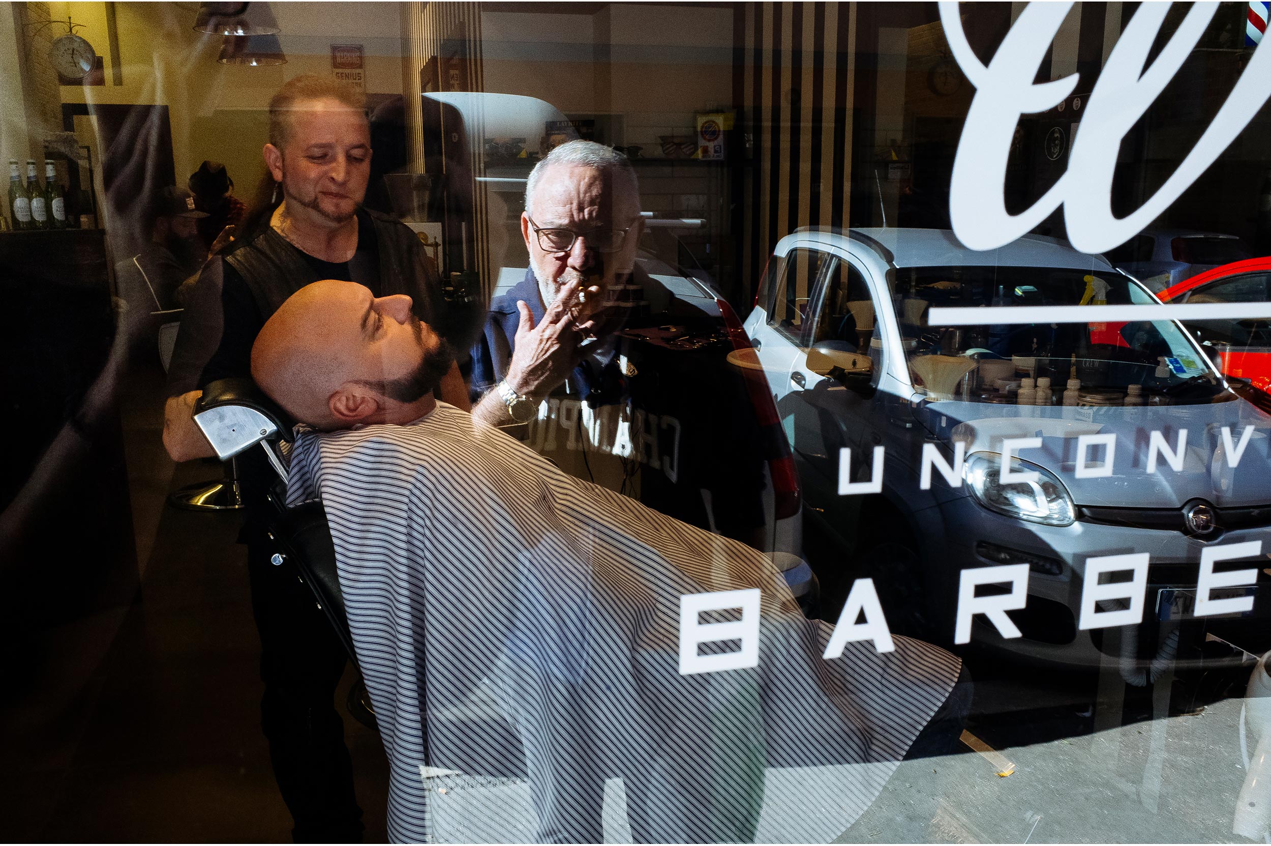 groom getting ready in the barbershop while his dad watches outside