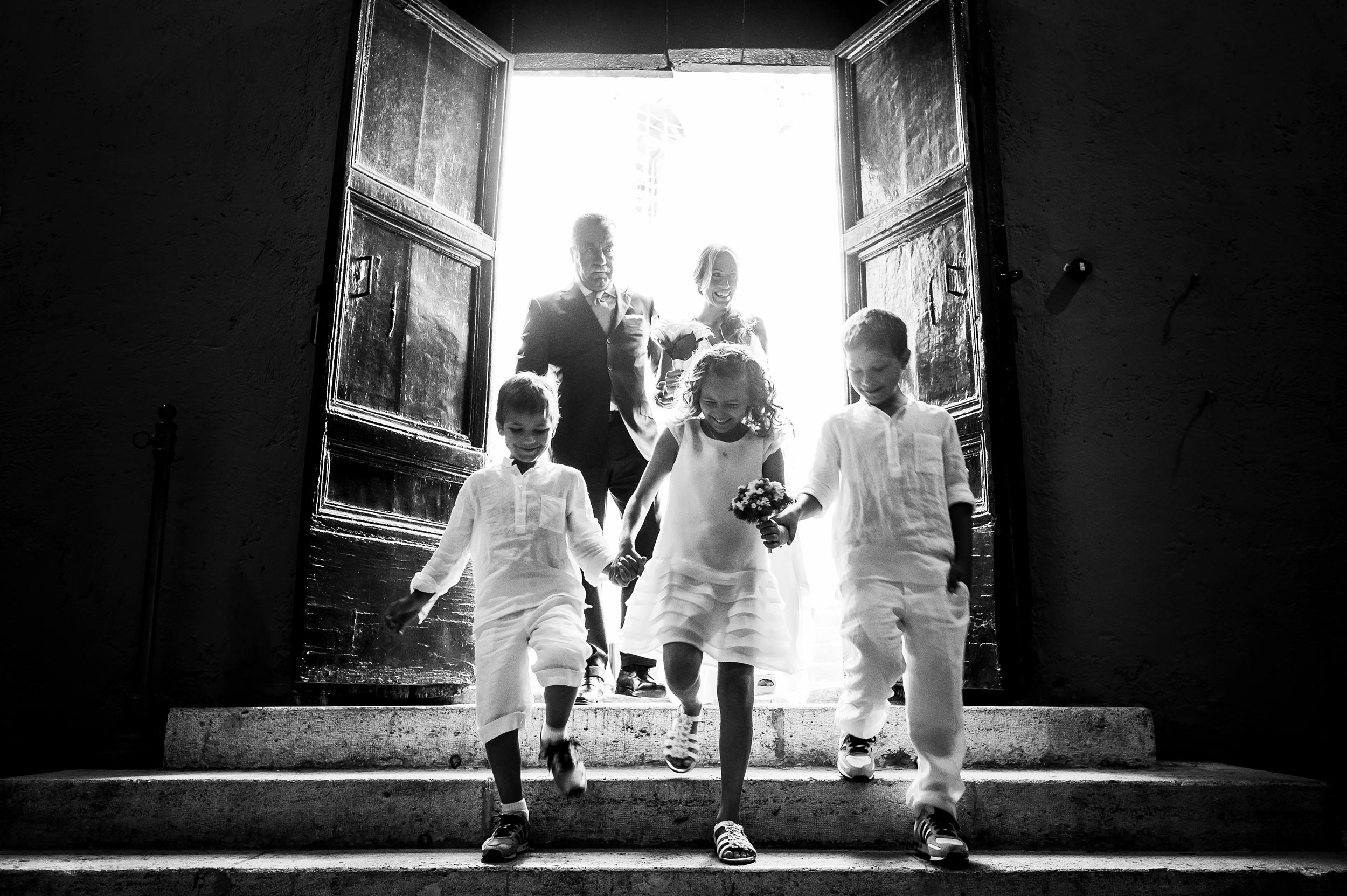 bride and dad enter church with three kids down the steps vatica city rome black and white wedding photography