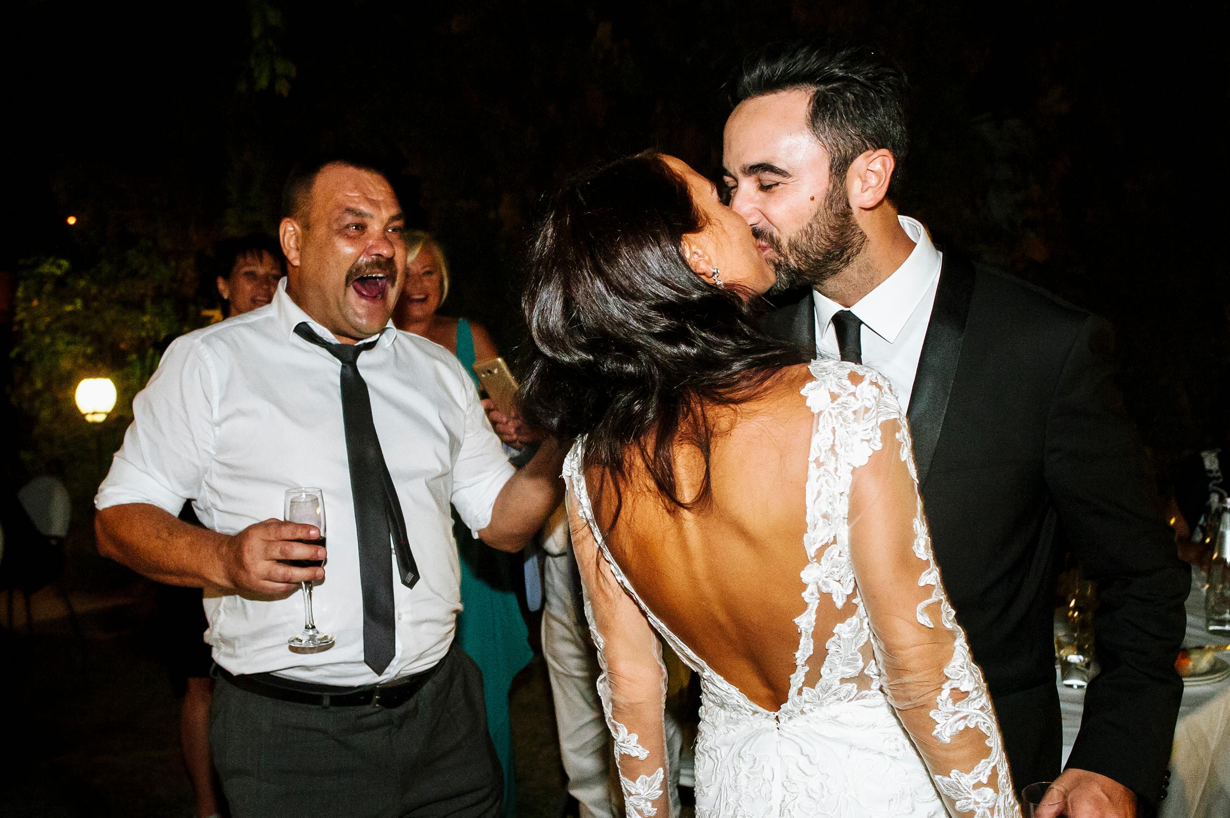 bride and groom kissing in front of brides father