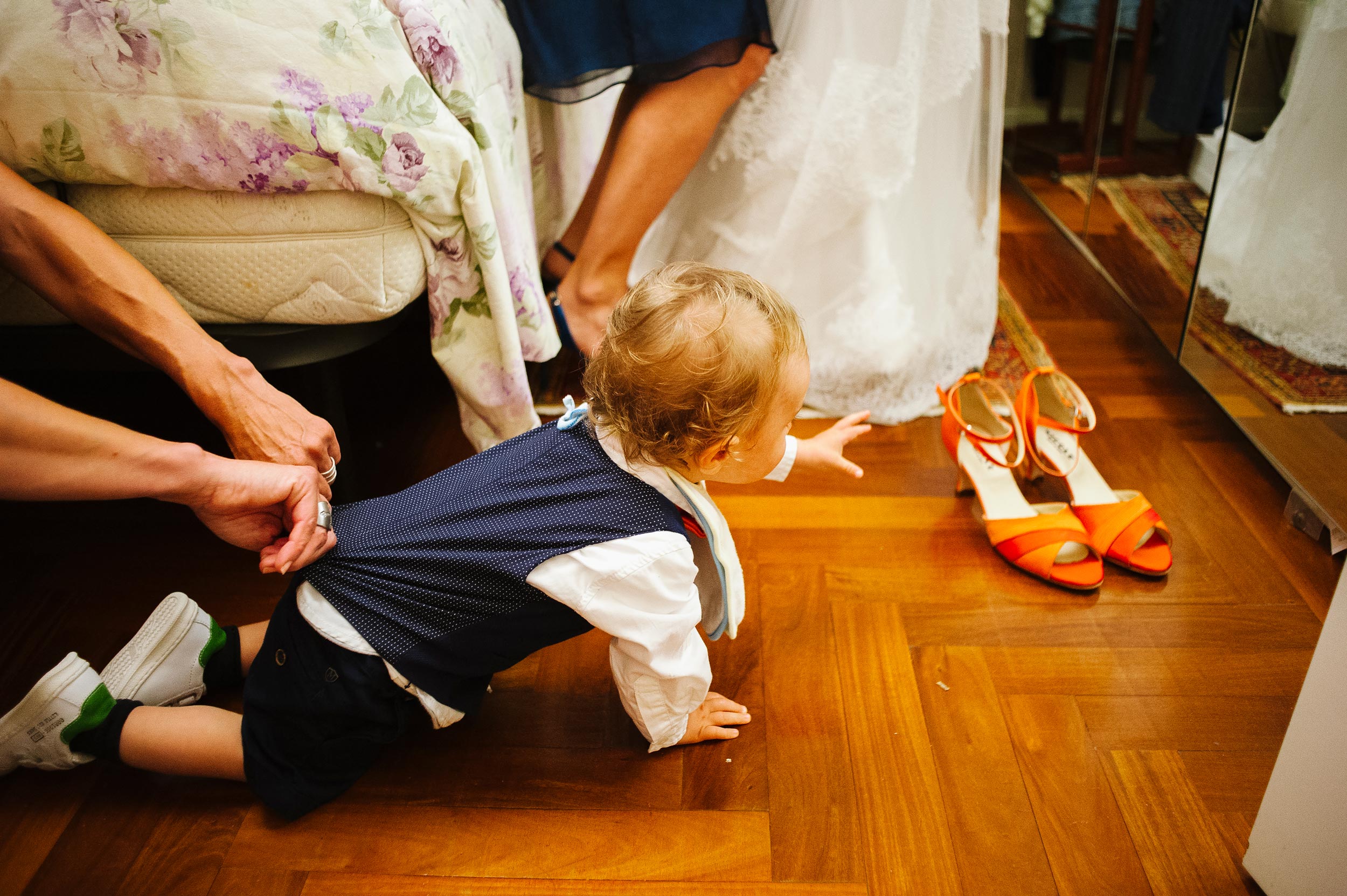 kid aims for brides shoes while his mom holds him