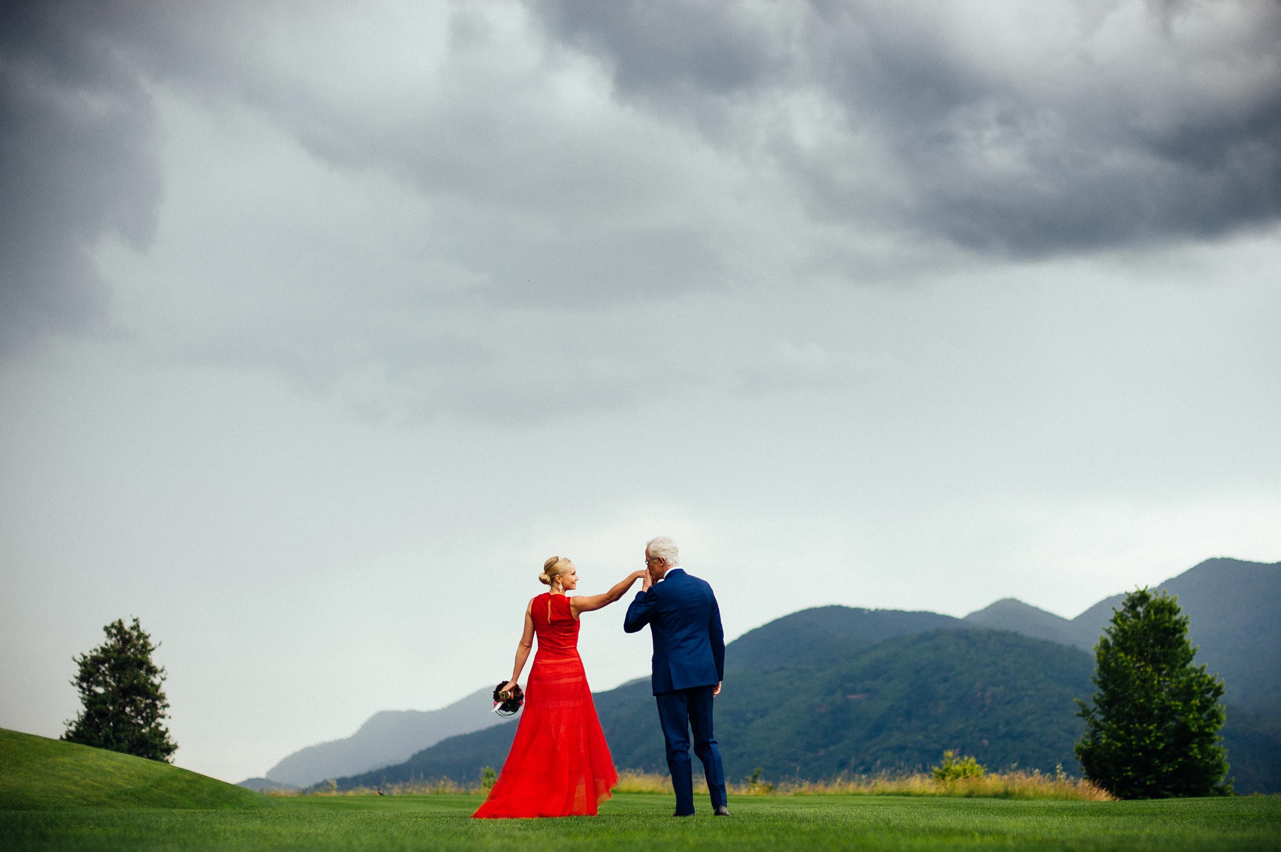 groom in blue kisses the bride with red wedding dress on a green grass field lugano switzerland